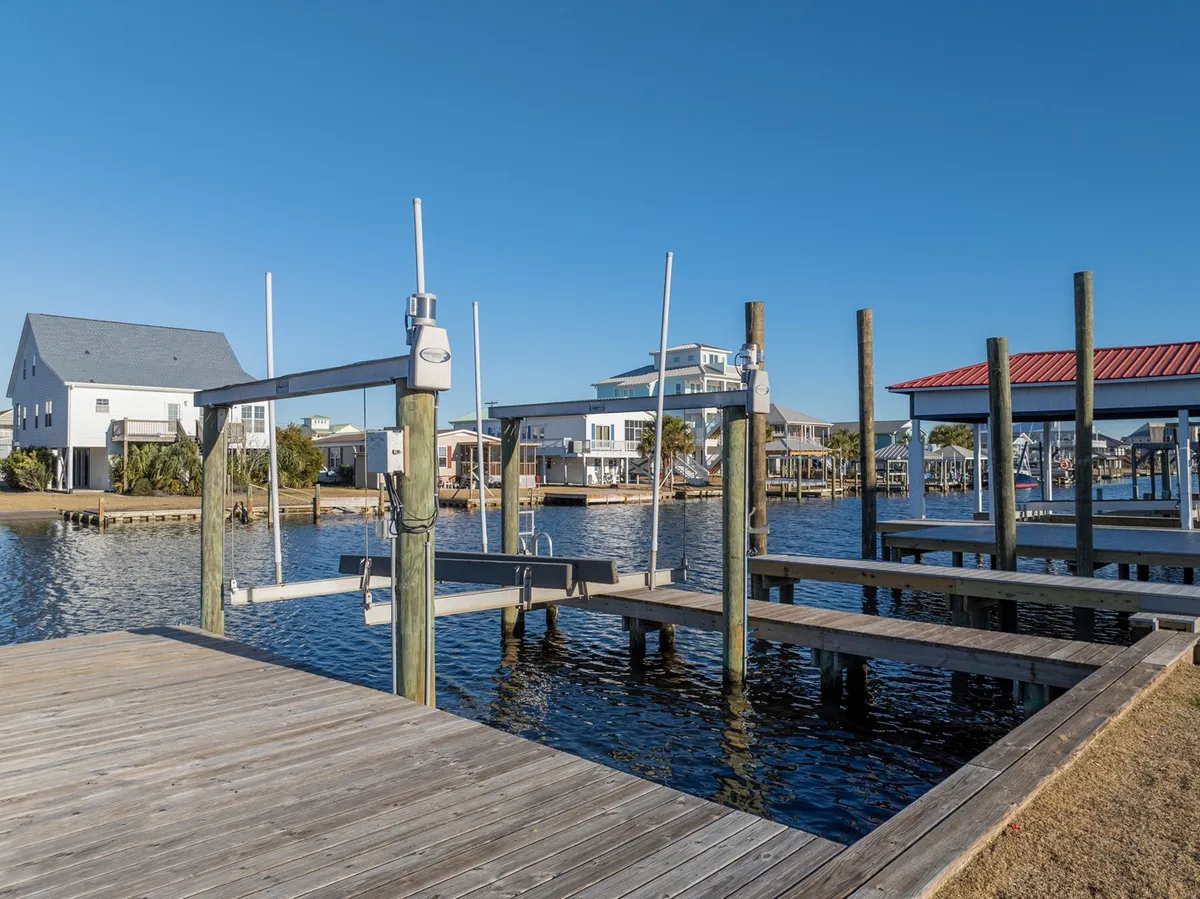 A wide-angle view of the waterway lined by docks, boats, and neighboring houses, with a spacious wooden dock extending over the calm canal waters. The image conveys social and leisure activities, as well as the potential for gathering with friends or family by the water's edge.