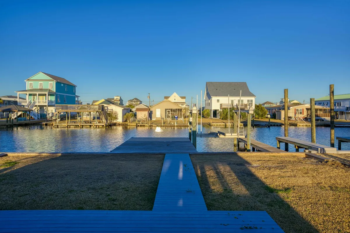 An exterior perspective showcasing the tranquil waterway, private dock, and boat lift, with surrounding homes in the distance. The image captures the allure of direct water access and the peaceful atmosphere of the setting.