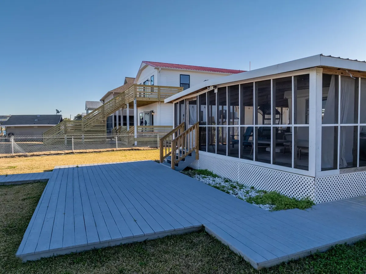 This exterior image highlights the home's screened porch, wooden deck with stairs leading up to the house, and a fenced yard. The entry appears easily accessible, with only a few steps and flat transitions, and the outdoor area looks inviting for both relaxing and gatherings. The scene conveys a welcoming and practical approach to indoor-outdoor living.