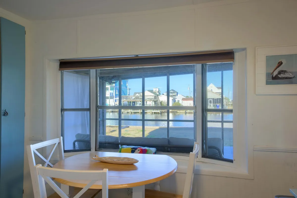 This image captures a dining table set next to a large window, with a clear view of an outdoor seating area. Sunlight streams in, drawing the eye outdoors and hinting at seamless indoor-outdoor living. The scene feels relaxed and inviting, encouraging guests to enjoy meals while gazing outside or to step directly onto the porch or deck area.