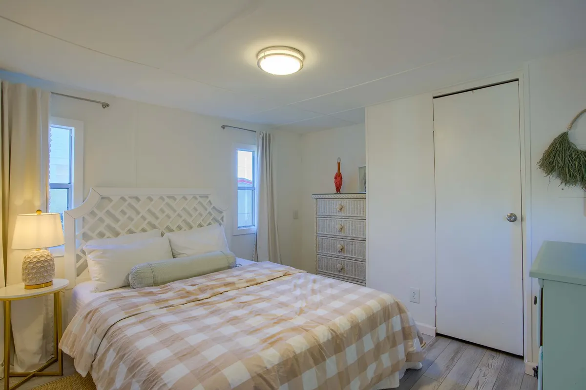 An inviting bedroom with a neatly made bed, lamp, dresser, and a decorative object on the dresser. The room is filled with soft, natural light, emphasizing the cozy and restful atmosphere.