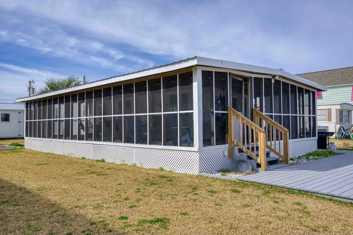 This image captures the home's spacious screened porch, complete with sturdy wooden stairs and a lawn area, offering a comfortable transition between indoor and outdoor living. The porch is inviting, furnished for relaxation or casual outdoor meals, and overlooks a tranquil canal, reinforcing the connection to natural surroundings and opportunities for wildlife viewing.