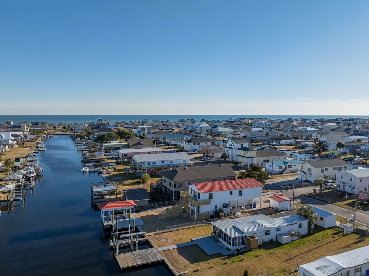This scenic exterior shot highlights the neighborhood’s canal, nearby houses, the distant ocean, and several boats moored along the water. The perspective emphasizes the close proximity to water and the vibrant coastal lifestyle, giving viewers a sense of the broader environment they’ll explore, including fishing, boating, and easy beach access.