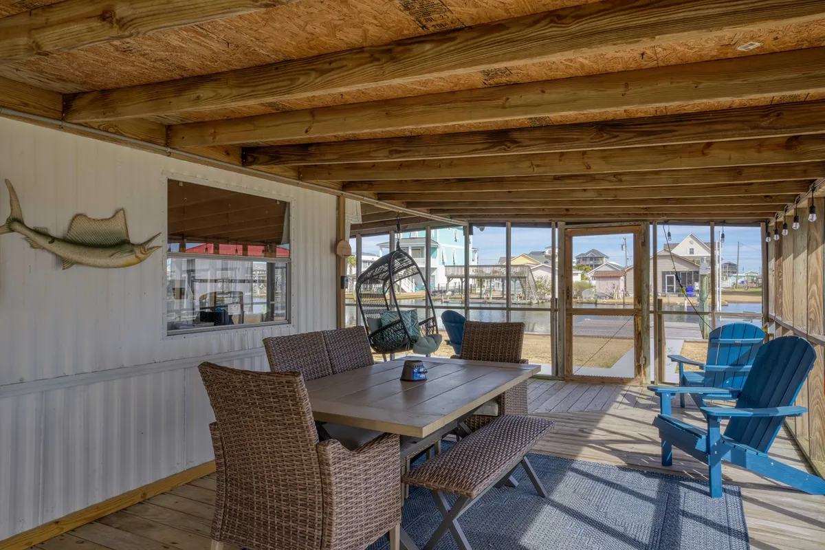 A cheerful, casually styled area featuring a dining table, blue Adirondack chairs, a unique hanging chair, and a playful fish wall decoration. The space is light and social, ideal for group dining or relaxed gatherings.