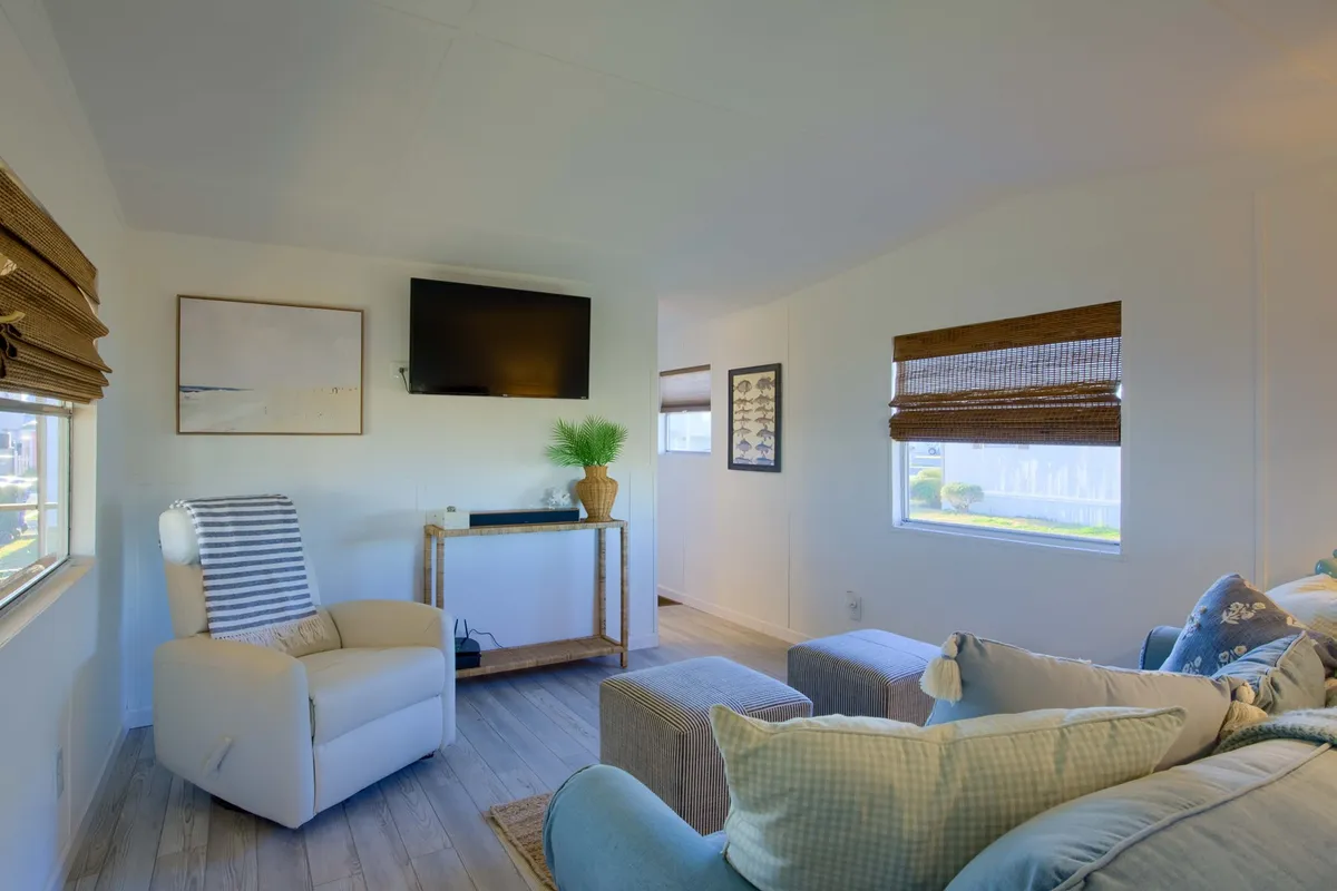 This interior image showcases a cozy living room with a comfortable armchair, a sofa adorned with decorative pillows, and a wall-mounted television—perfect for relaxing, socializing, or enjoying movie nights. The space is welcoming and arranged for comfort, echoing the heart of a cottage-themed home.